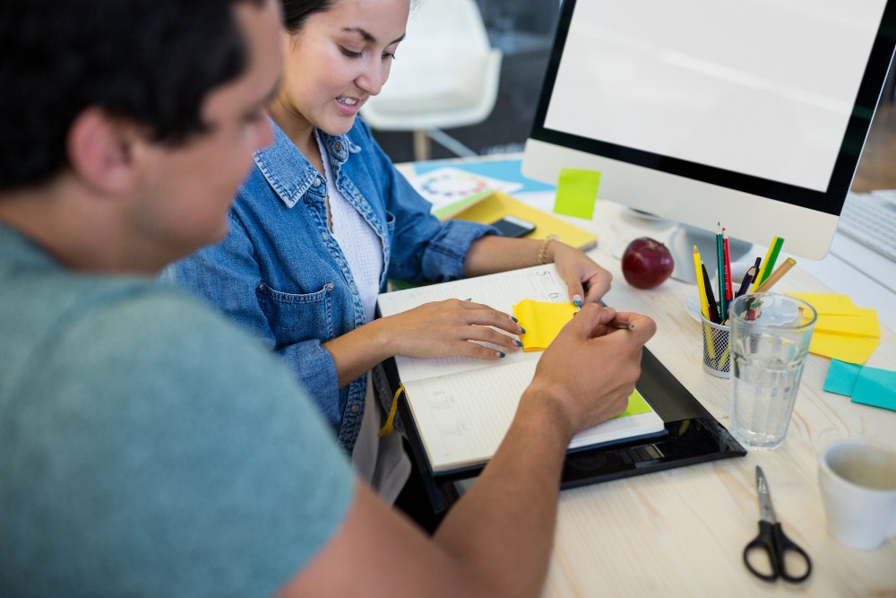 Dois colegas de trabalho colando post it em uma agenda e fazendo anotações.