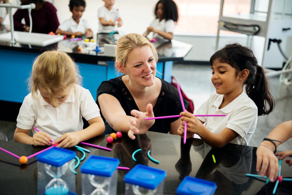Professora em laboratório de robótica ensinando alunos do ensino fundamental.