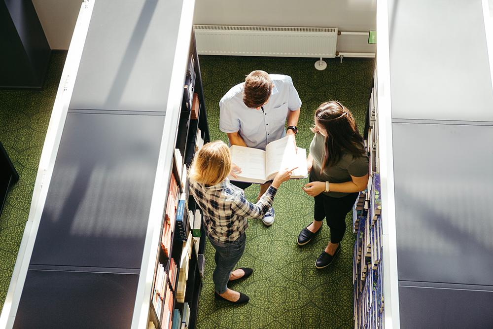 Alunos em biblioteca folheando livro.