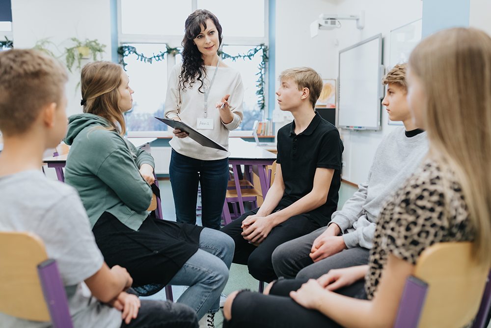 Professora conversando sobre saúde mental na escola com um grupo de alunos.