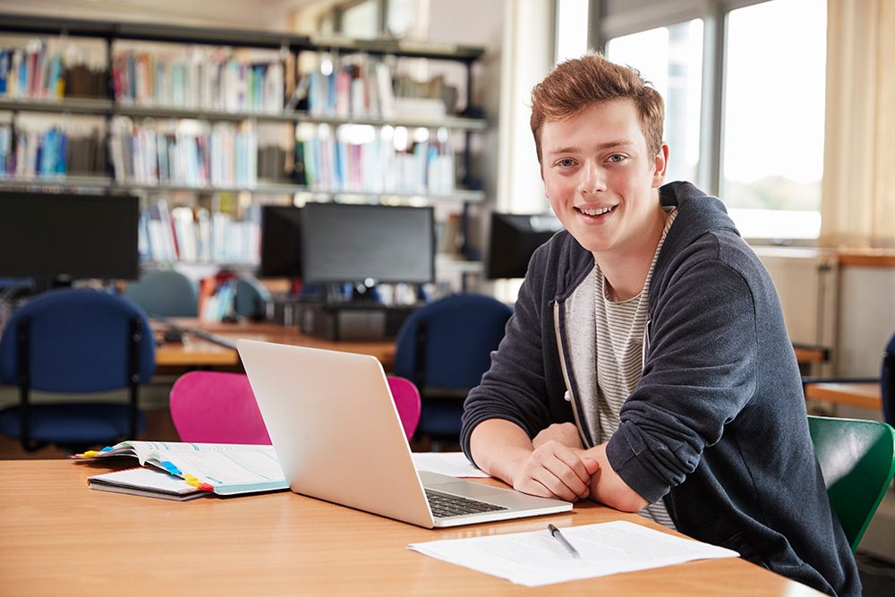 Jovem estudante usando computador em uma biblioteca.