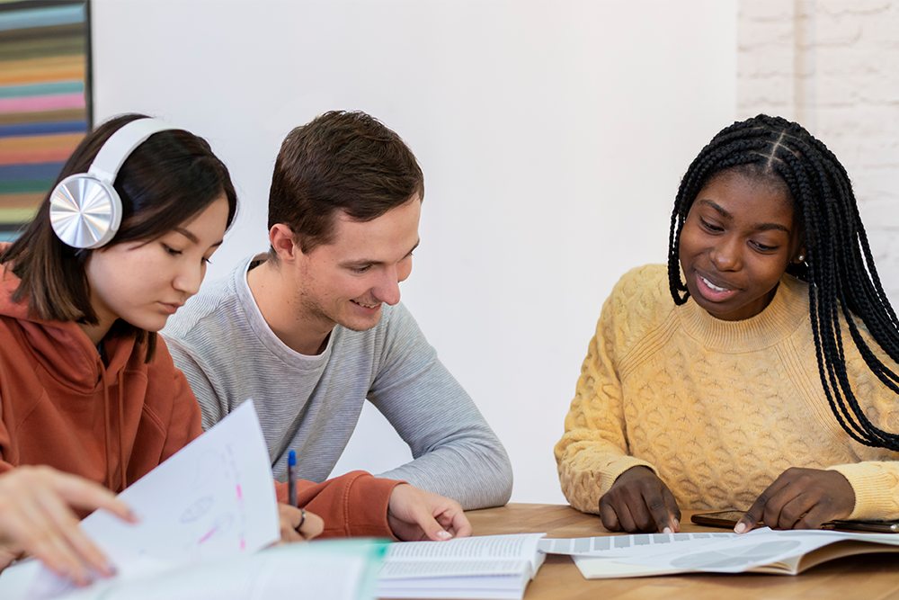 Três estudantes na biblioteca conversando e estudando juntos.