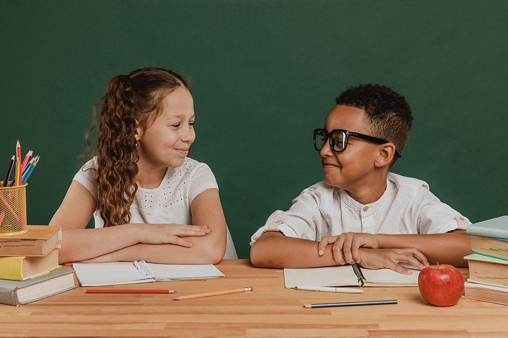 Menino em menina em sala de aula se entreolhando enquanto sorriem.