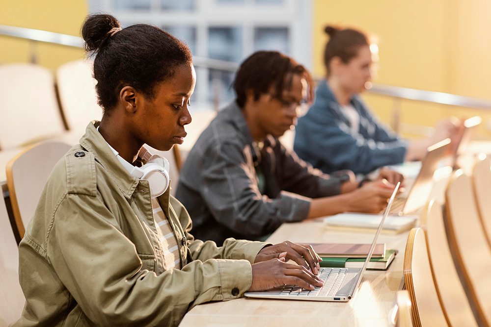 Jovens estudantes em sala de aula usando computador para estudar.