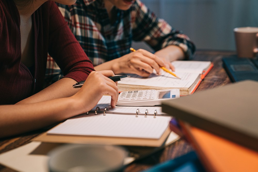 Duas estudantes usando calculadora e caderno de anotações para estudar para o vestibular.