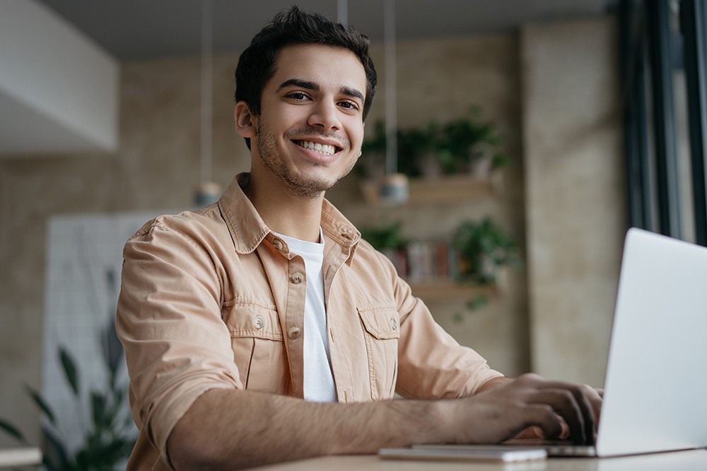Aluno do ensino médio digitando no computador e sorrindo.